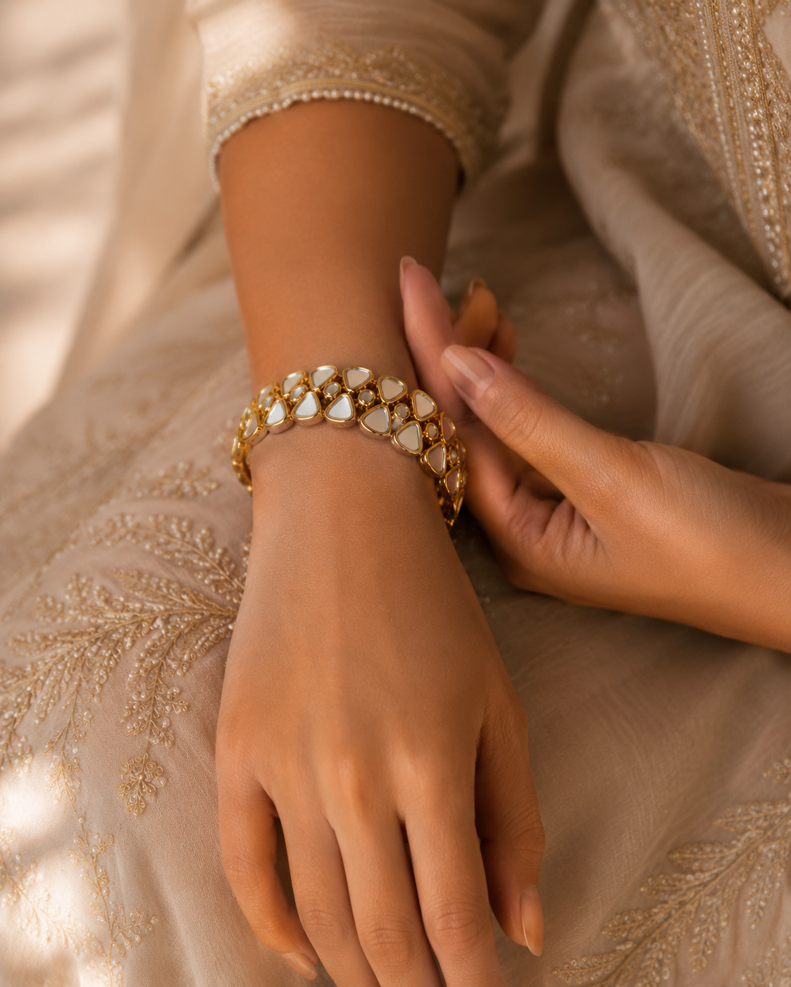 Close-up of a hand wearing a gold bracelet with pearls on a beige fabric background