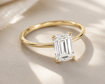 Gold ring with a rectangular diamond on a beige fabric background