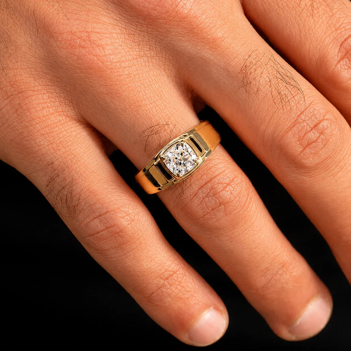 A close-up of a hand wearing a yellow gold ring with a rectangular cushion-cut diamond. The ring features a polished gold band and a bezel-set diamond center stone.