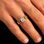 A close-up of a hand wearing a yellow gold ring with a rectangular cushion-cut diamond. The ring features a polished gold band and a bezel-set diamond center stone.