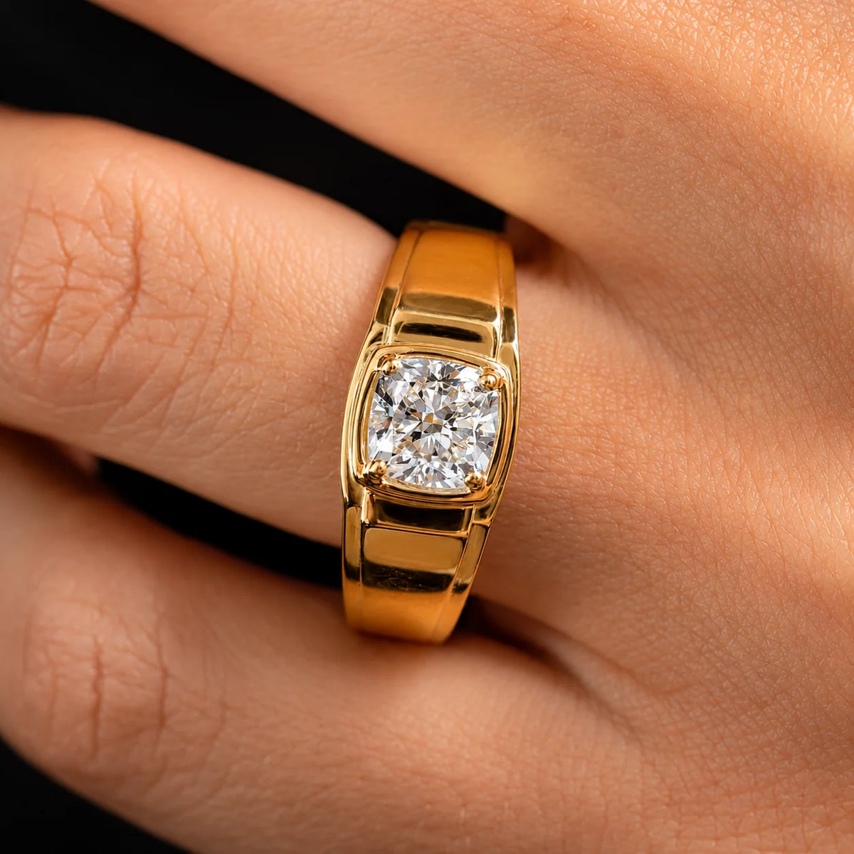 A close-up of a gold ring with a square cushion-cut diamond set on a person's finger against a dark background.