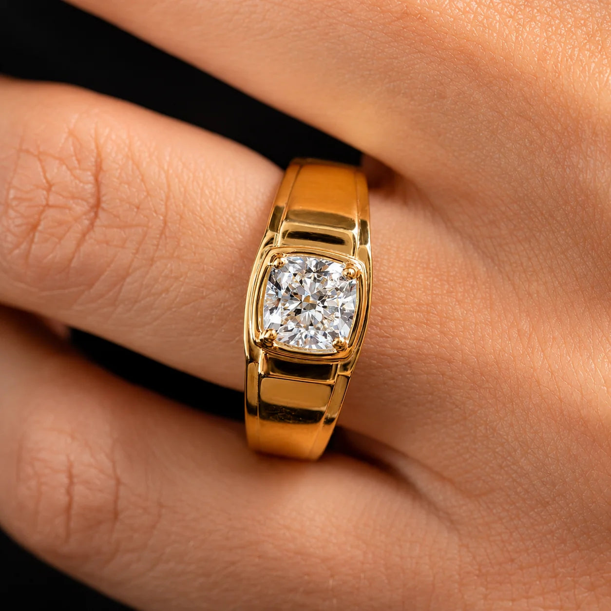 A close-up of a gold ring with a square cushion-cut diamond set on a person's finger against a dark background.