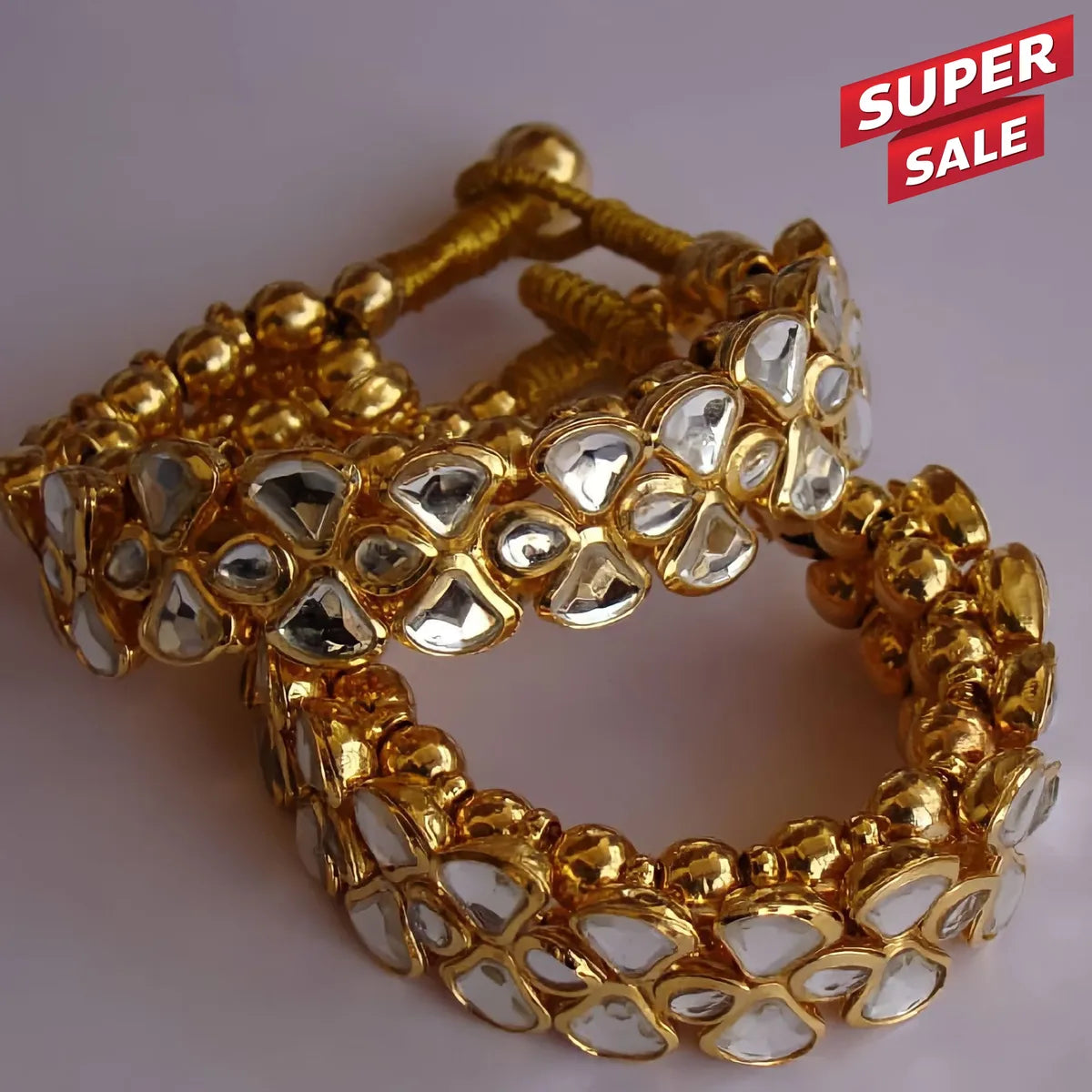 Three gold-plated Kundan bangles with white inlaid stones, displayed on a neutral light gray background with a red 'SUPER SALE' promotional sticker in the top right corner.