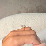 Gold ring with a heart-shaped diamond held between fingers against a neutral background