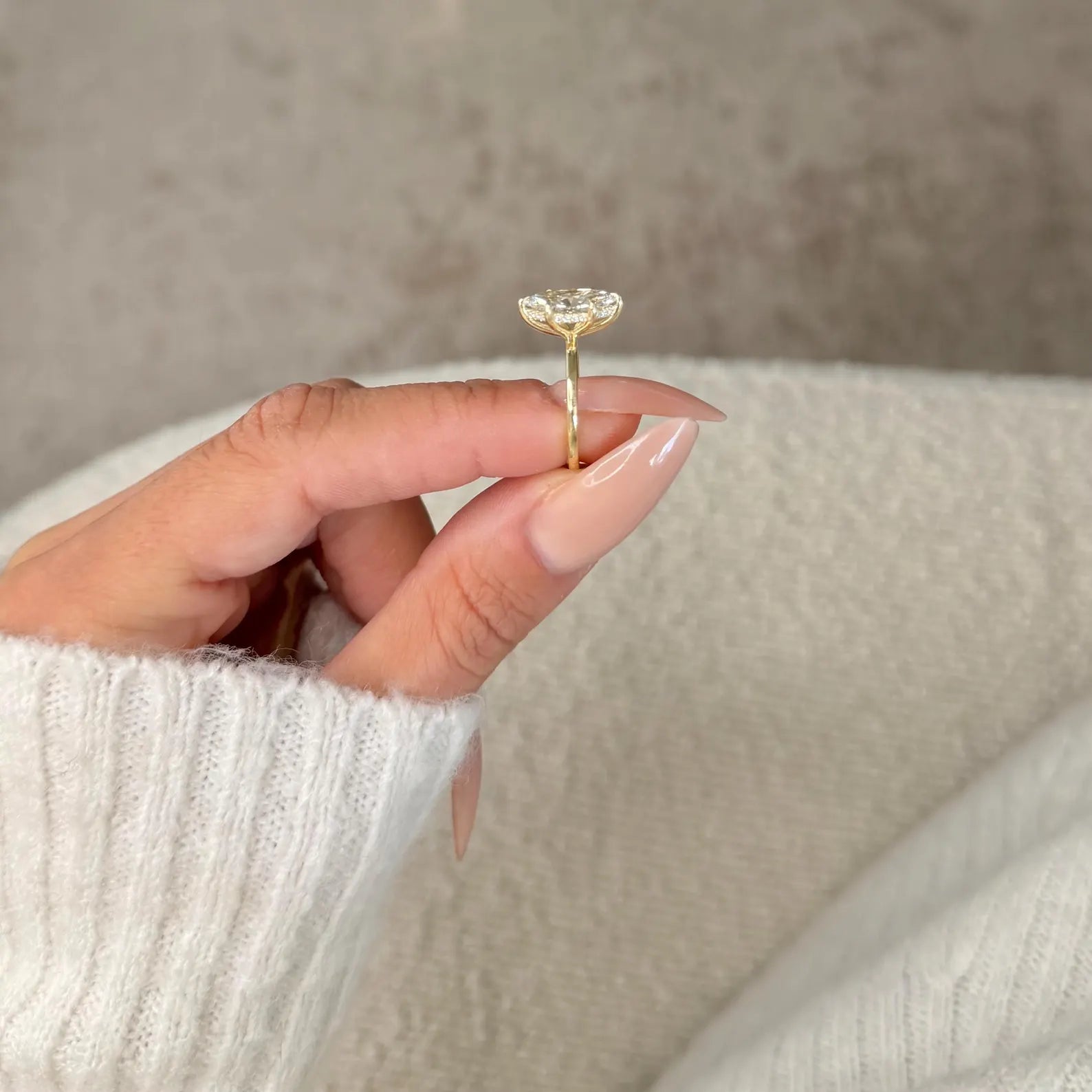 Hand holding a gold ring with a clear gemstone against a neutral background