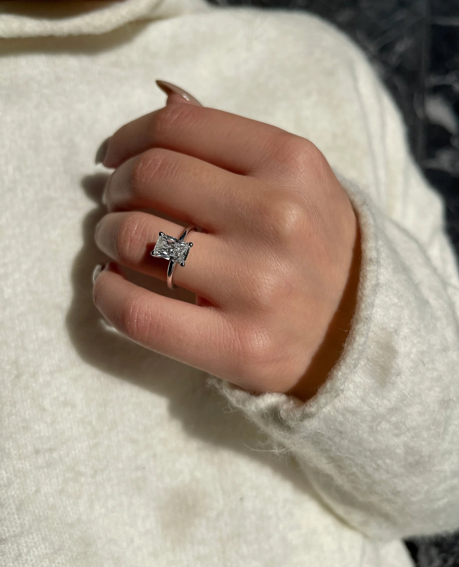 Hand wearing a silver ring with a diamond on a light background