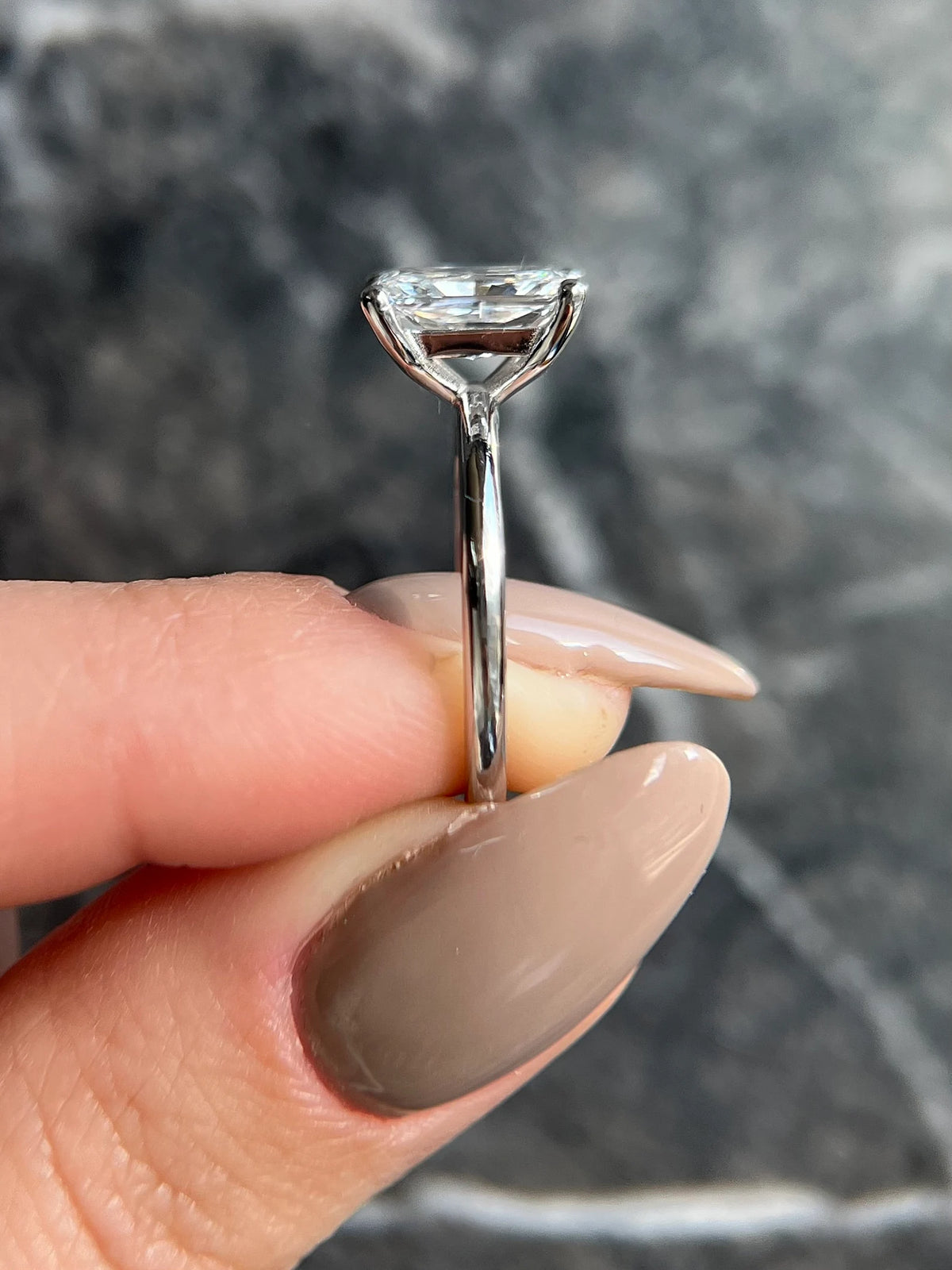 Silver ring with a diamond held between fingers against a gray stone background