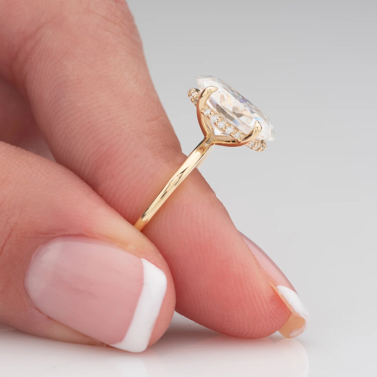 Gold ring with a large diamond held between fingers on a neutral background