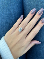 A close-up of a hand with mauve-colored nails wearing a silver ring with a large clear gemstone, resting against blue denim fabric.