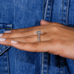 A close-up of a hand wearing a silver-toned diamond engagement ring, resting against a blue denim jacket.