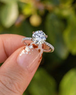 Diamond ring held by a hand with a blurred green background